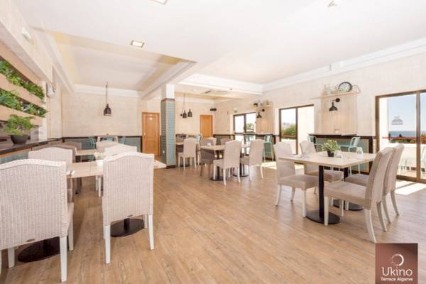 Innenansicht des Restaurants Ukino Terrace Algarve mit Holzboden, modernen Tischen und Stühlen sowie großen Fenstern.