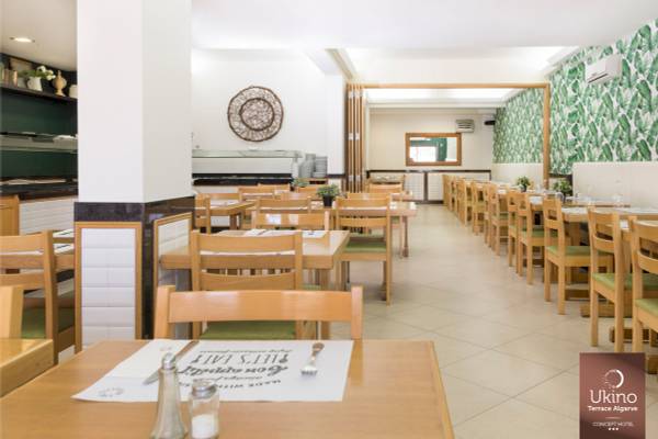 Innenansicht des Restaurants Ukino Terrace Algarve mit runden Tischen und Stühlen, weißen Wänden und grünen Tapeten.
