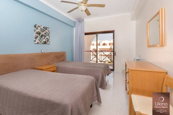 Schlafzimmer im Ukino Terrace Algarve Hotel mit zwei Betten, Deckenventilator und Zugang zur Terrasse.