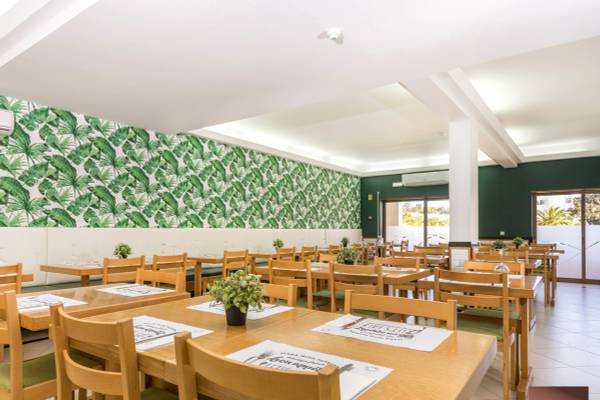Innenbereich des Restaurants im Ukino Terrace Algarve Hotel mit grünen Blattmustern an der Wand und runden Holztischen.