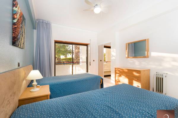Innenansicht eines Doppelzimmers im Ukino Terrace Algarve Hotel mit zwei Betten, Nachttischen, Deckenventilator und Fenstern.