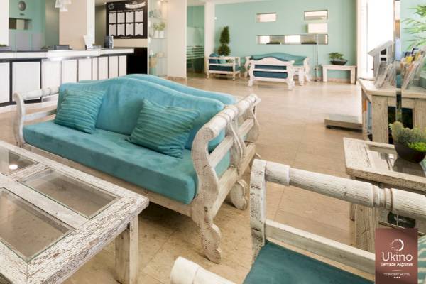 Lobby des Ukino Terrace Algarve Hotels mit blauen Sofas und weißen Holztischen.