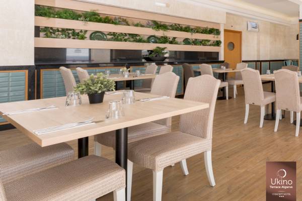 Innenbereich des Restaurants im Ukino Terrace Algarve Hotel mit Tisch und Stühlen, grünen Pflanzen und Holzboden.