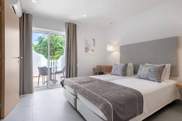 Doppelbett-Zimmer mit Balkon im Ancora Park Hotel, modernes Design mit weißer Wand, Glastür und grüner Vorhang.