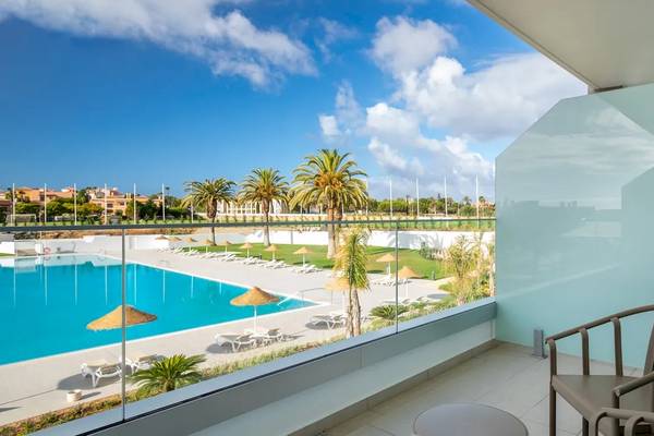 Aussicht von einem Hotelzimmer auf einen Swimmingpool und einen Loungebereich mit Sonnenliegen und Palmen.