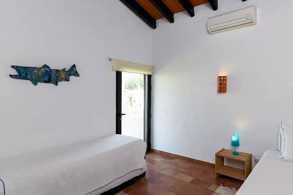 Zwei Betten im Zimmer des Pedras da Rainha Resort mit weißen Wänden, Holzboden und dekorativen Elementen.