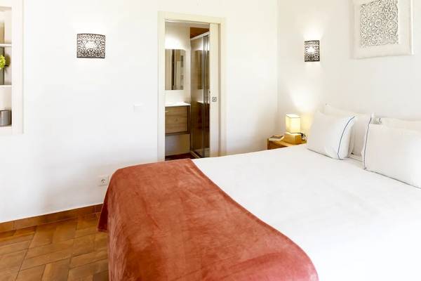 Ein modernes Hotelzimmer mit einem großen Bett, weißen Wänden und Holzboden, mit Blumen und Leuchten als Dekoration.