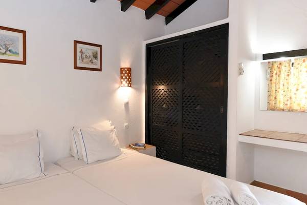 Schlafzimmer im Pedras da Rainha Resort mit zwei weißen Betten und schwarzen Türen.