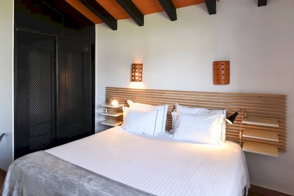 Innenansicht eines Schlafzimmers im Pedras da Rainha Resort mit einem Bett, weißen Kissen, und schwarzen Möbeln.