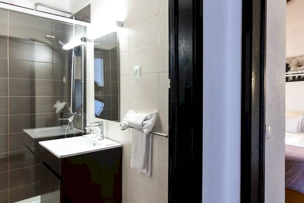 Innenansicht eines Zimmers im Pedras da Rainha Resort mit separatem Badezimmer, Bett, Nachttisch und Lampe.