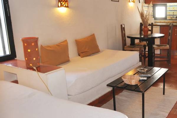 Innenraum des Pedras da Rainha Resorts mit Sofa, Tisch, Lampe und Küche im Hintergrund.