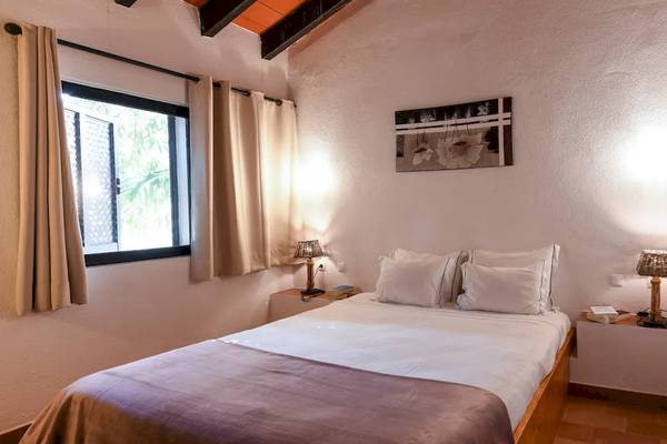 Innenansicht eines Schlafzimmers im Pedras da Rainha Resort mit einem Bett, zwei Nachttischen, Lampen und einem Fenster.