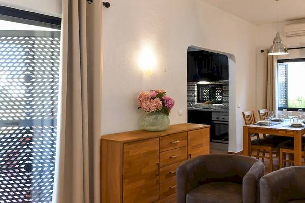 Innenansicht des Pedras da Rainha Resorts mit Esstisch, Blumenvase, Schrank und Küche im Hintergrund.