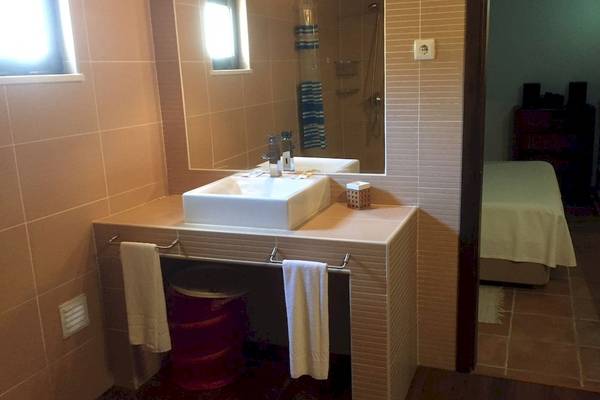 Ein Badezimmer mit einem Waschbecken, Spiegel und einem Bett im Hintergrund.