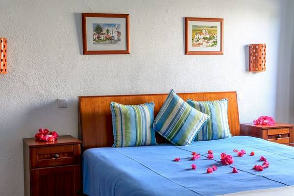 Schlafzimmer im Pedras da Rainha Resort mit Rosenblättern auf dem Bett und dekorativen Bildern an der Wand.