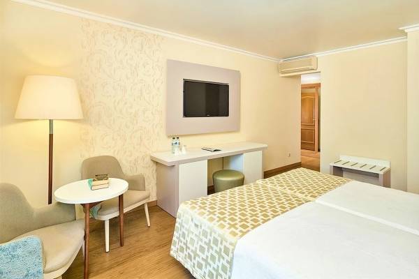 Innenansicht eines Doppelzimmers im Baia Grande Hotel mit zwei Betten, einem Schreibtisch und einem Fernseher an der Wand.