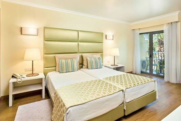 Doppelbett-Zimmer im Baia Grande Hotel mit grünem Kopfteil und Balkonzugang.