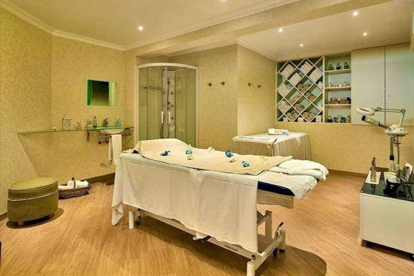 Behandlungsraum im Baia Grande Hotel mit zwei Behandlungstischen, einer Dusche und Regalen mit Wellnessartikeln.