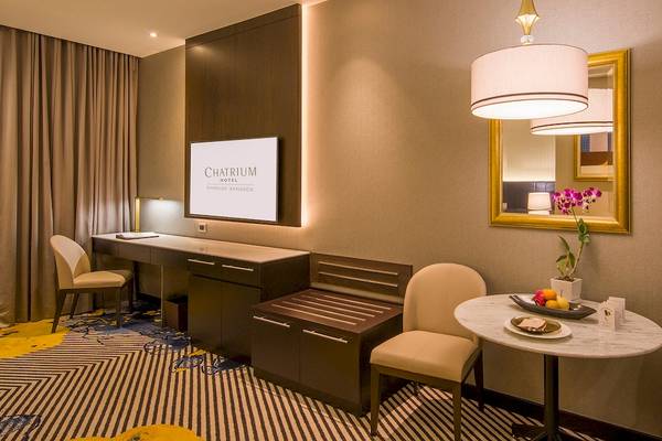 Innenansicht eines Zimmers im Chatrium Hotel Riverside Bangkok mit Schreibtisch, Stühlen und Tisch.