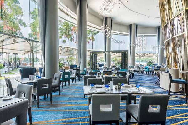 Innenansicht des Restaurants im Chatrium Hotel Riverside Bangkok mit blauen Teppichboden und modernen Möbeln.