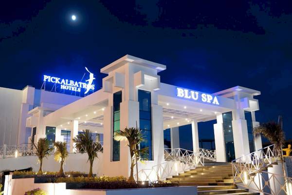 Nachtansicht des Pickalbatros Blu Spa Resort Hotels mit voll beleuchtetem Gebäude und Palmen davor.