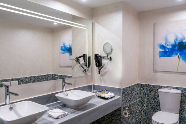 Badezimmer im Pickalbatros Blu Spa Resort mit zwei Waschbecken, Toilette und einer blauen Wandmalerei.