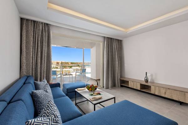 Wohnzimmer des Pickalbatros Blu Spa Resorts mit blauer Couch, Tisch und Aussicht auf den Pool.