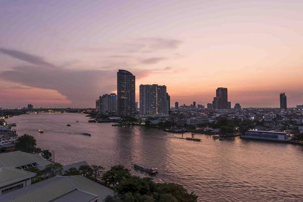 Aussicht auf Chatrium Hotel Riverside Bangkok bei Sonnenuntergang mit Fluss, Booten und Gebäuden