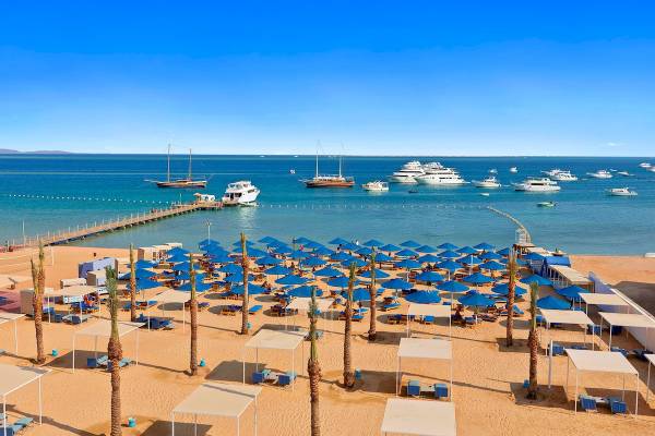 Luftaufnahme des Pickalbatros Blu Spa Resorts Strands mit vielen blauen Sonnenschirmen und Booten im Hintergrund.