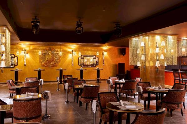 Innenansicht des Restaurants im Pickalbatros Blu Spa Resort mit runden Tischen, Stühlen und dekorativen Wandleuchten.