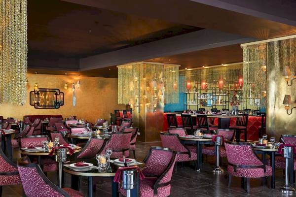 Innenansicht des Restaurants im Pickalbatros Blu Spa Resort mit runden Tischen, roten Stühlen und goldenen Vorhängen.