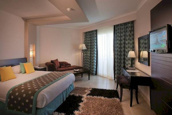Ein modernes Hotelzimmer im Amwaj Beach Club mit Bett, Sofa, Schreibtisch, Fernseher und Lampen.