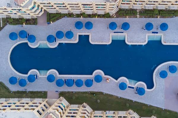 Luftaufnahme des Amwaj Beach Club Hotels mit großem Pool und blauen Sonnenschirmen.