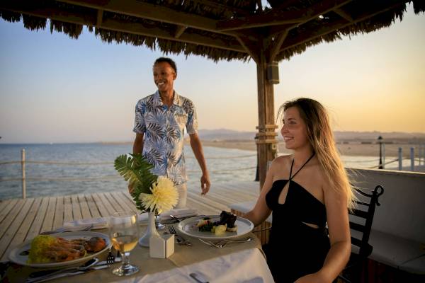 Gast genießt ein Essen auf der Terrasse des Amwaj Beach Club bei Sonnenuntergang.