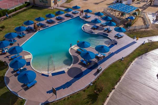 Luftaufnahme des Amwaj Beach Club mit großem Schwimmbad und vielen blauen Sonnenschirmen.