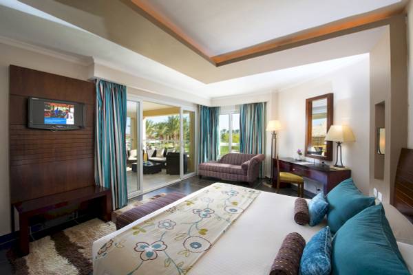 Innenansicht eines Zimmers im Amwaj Beach Club Hotel mit großem Bett, Fernseher und Balkon.