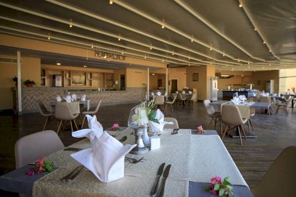 Innenraum des Amwaj Beach Club Restaurants mit gedeckten Tischen und Stühle, Blumenarrangements und eine Theke.