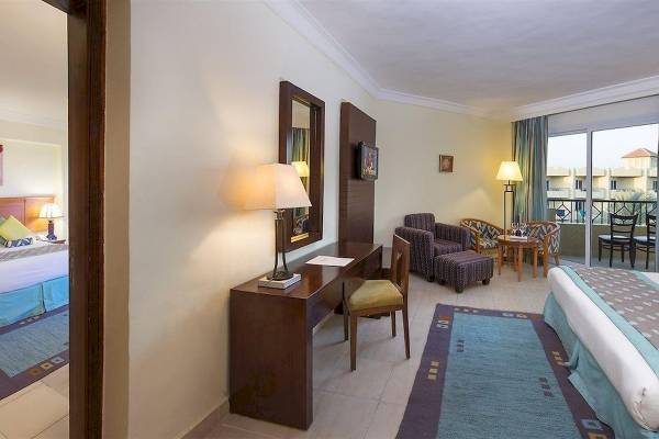 Innenansicht eines Hotelzimmers im Amwaj Beach Club mit Schreibtisch, Stühlen, Bett und Balkon.