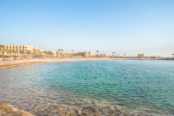 Strand des Pickalbatros Aqua Vista Resorts mit Gebäuden und Palmen im Hintergrund.