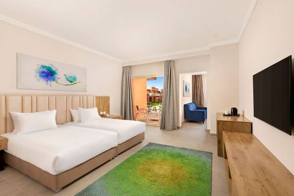 Innenansicht eines Zimmers im Pickalbatros Water Valley Resort by Neverland mit zwei Betten, Fernseher, Tisch und Sofa.