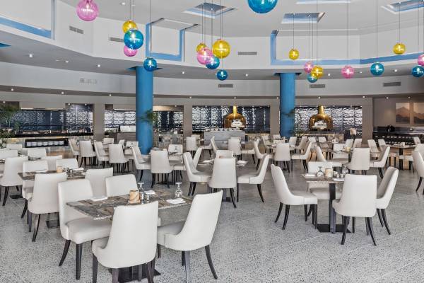 Innenansicht des Restaurants im Pickalbatros Water Valley Resort by Neverland mit vielen Tischen und Stühlen, farbigen Deckenleuchten und blauen Säulen.