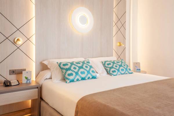 Schlafzimmer im Grupotel Los Principes & Spa mit einem Bett, zwei blauen Kissen und einer Lampe an der Wand.