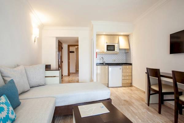Innenansicht einer Hotelsuite im Grupotel Los Principes & Spa mit Wohnzimmer, Schlafbereich, Küche und Essbereich.