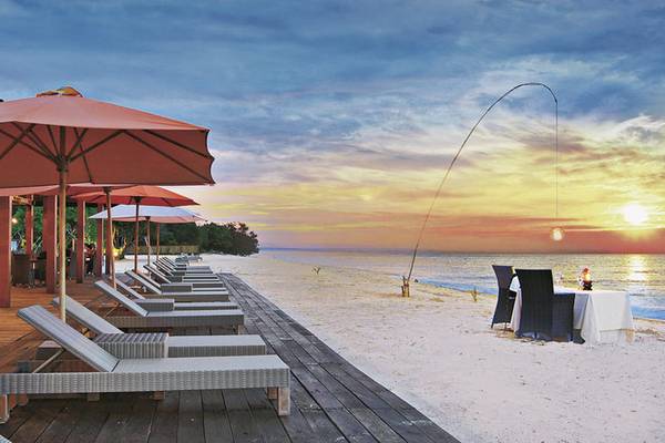Strandszene mit Sonnenuntergang, Sonnenschirmen und Lounge-Sesseln im Jimbaran Puri, Bali.