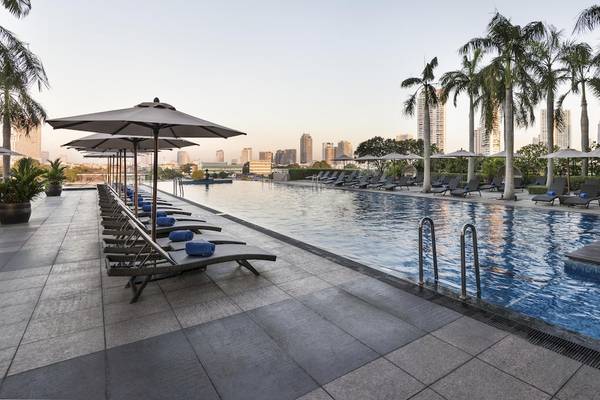 Loungebereich mit Sonnenliegen und Schirmen am Pool des Chatrium Hotel Riverside Bangkok.