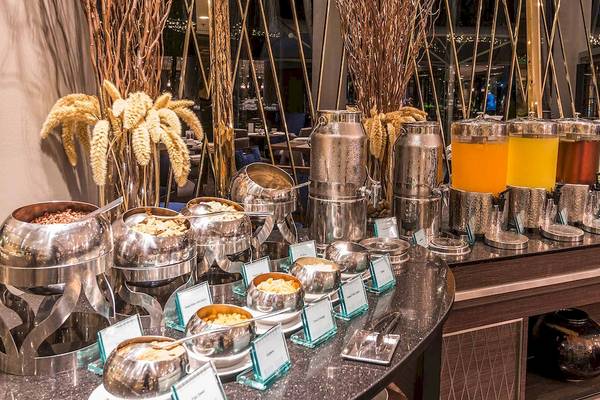 Buffetstation im Chatrium Hotel Riverside Bangkok mit verschiedenen Getränken und Speisen in silbernen Behältern.