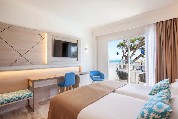 Innenansicht eines Hotelzimmers mit Schreibtisch, zwei Betten und Blick auf den Strand.