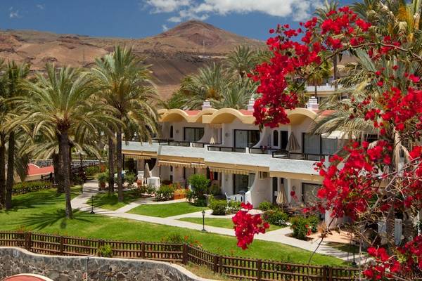Außenansicht des Grupotel Los Principes & Spa Hotels mit roten Blumen und Palmen im Vordergrund.