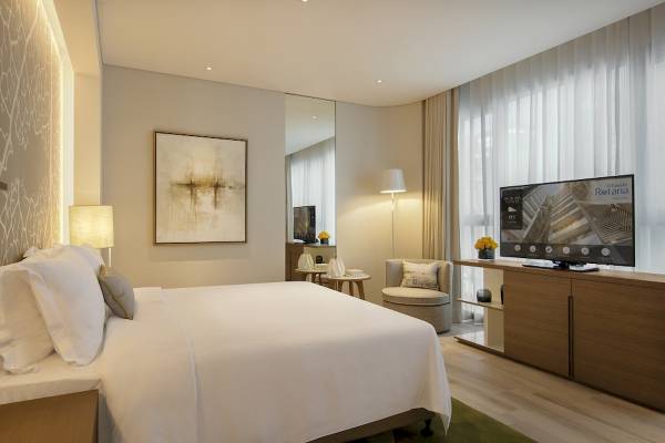 Hotelzimmer im Al Bandar Rotana mit großem Bett, Fernseher und Kunstwerk an der Wand.