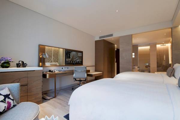 Zwei Betten in einem eleganten Hotelzimmer des Al Bandar Rotana, mit Schreibtisch und moderner Einrichtung.